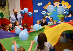 Na zdjęciu Burmistrz oraz dzieci z przedszkola podczas zabawy chustą animacyjną