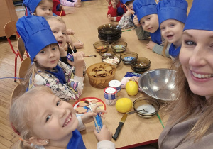 Na zdjęciu Pani KASIA wraz z Niezapominajkami, ubrani w niebieskie fartuchy i czapki kucharzy.