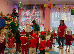 Na zdjęciu dzieci ubrane w czerwone świąteczne bluzeczki, śpiewają piosenkę dla Mikołaja
