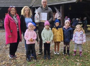 Na zdjęciu dzieci wraz z panią Dyrektor oraz Panią Anitą wręczają prezent panu leśniczemu