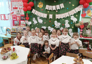 Na zdjęciu dziewczynki wraz z panią Kasią i Dominiką na tle czerwono- zielonej dekoracji, ubrane w stroje góralskie