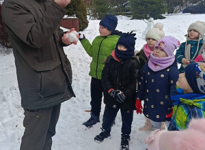 Na zdjęciu Pan Leśniczy trzymający w rękach pokarm dla ptaków, w tle widać wsłuchane dzieci