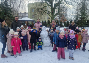 Na zdjęciu dzieci wraz z paniami i panem leśniczym, pomiędzy stoi ulepiony bałwan