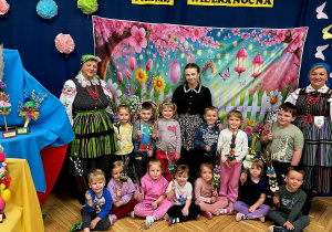 Na zdjęciu dzieci wraz z paniami, na tle dekoracji w dłoniach trzymają wykonane palmy