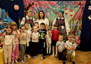 Na zdjęciu dzieci wraz z paniami, na tle dekoracji w dłoniach trzymają wykonane palmy