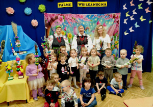 Na zdjęciu dzieci wraz z paniami, na tle dekoracji w dłoniach trzymają wykonane palmy
