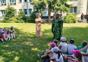 na zdjęciu widać dzieci, ktore siedzą na kocach, słuchają co opowiada im pani Kasia